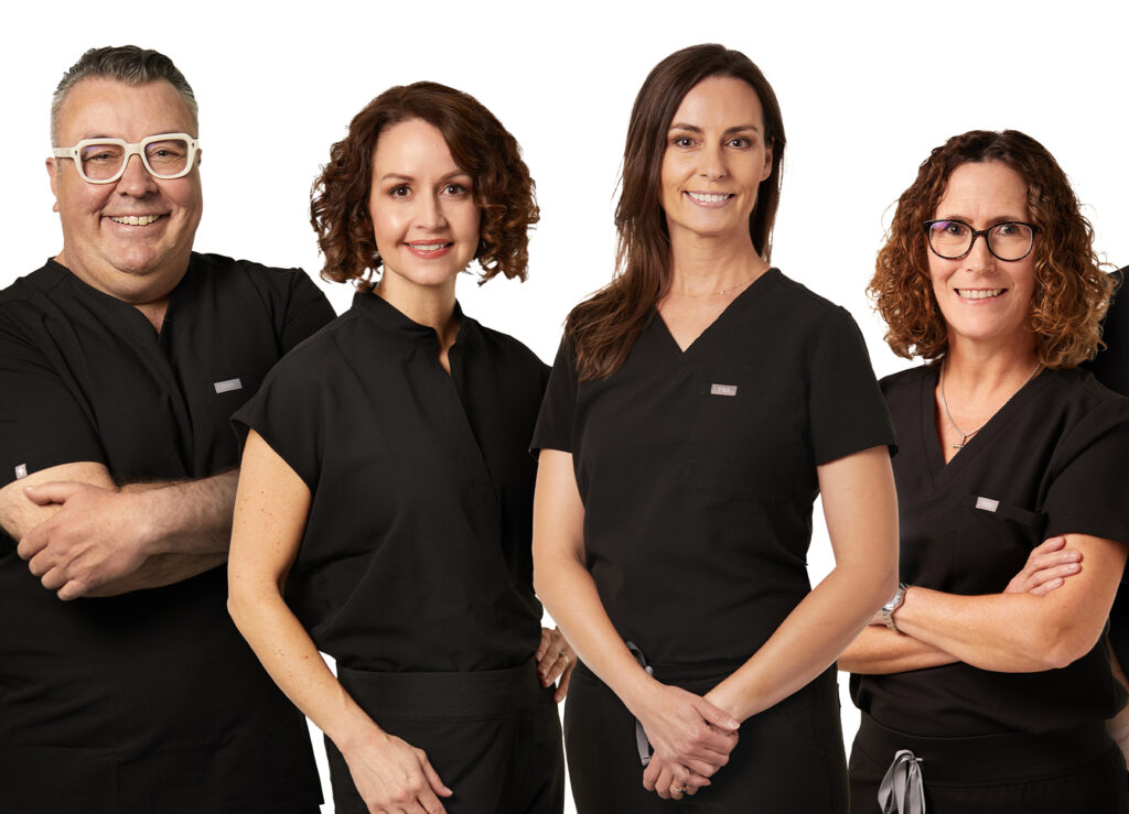 Four Tulsa OB-GYN physicians in black scrubs pose for a group photo in front of a white backdrop